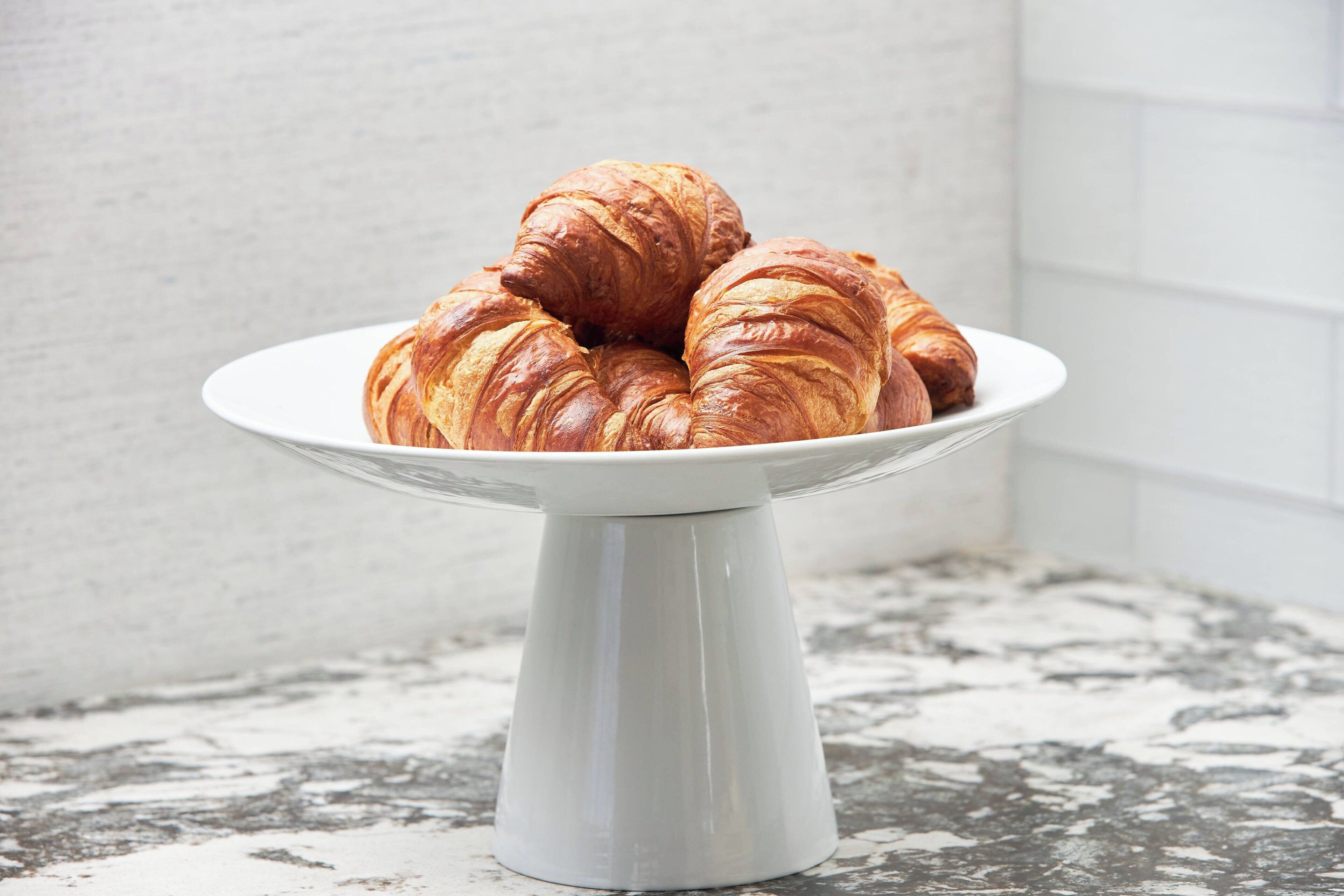 A white ceramic plate holding three croissants on a marble countertop.