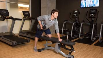 Un gimnasio con cintas de correr, elípticas y una banca para levantamiento de pesas.