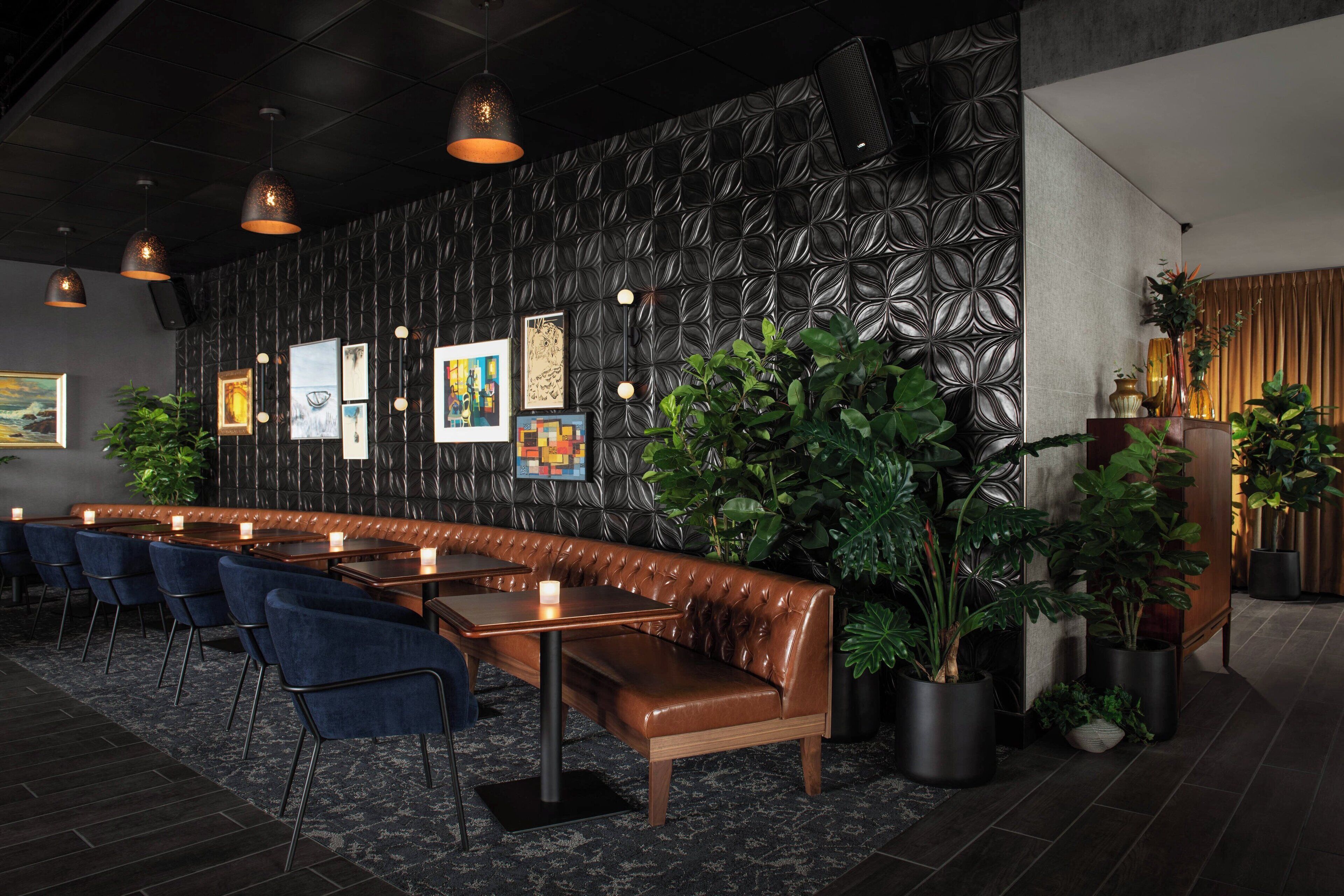 A modern restaurant with a long counter, blue chairs, and a leather booth.
