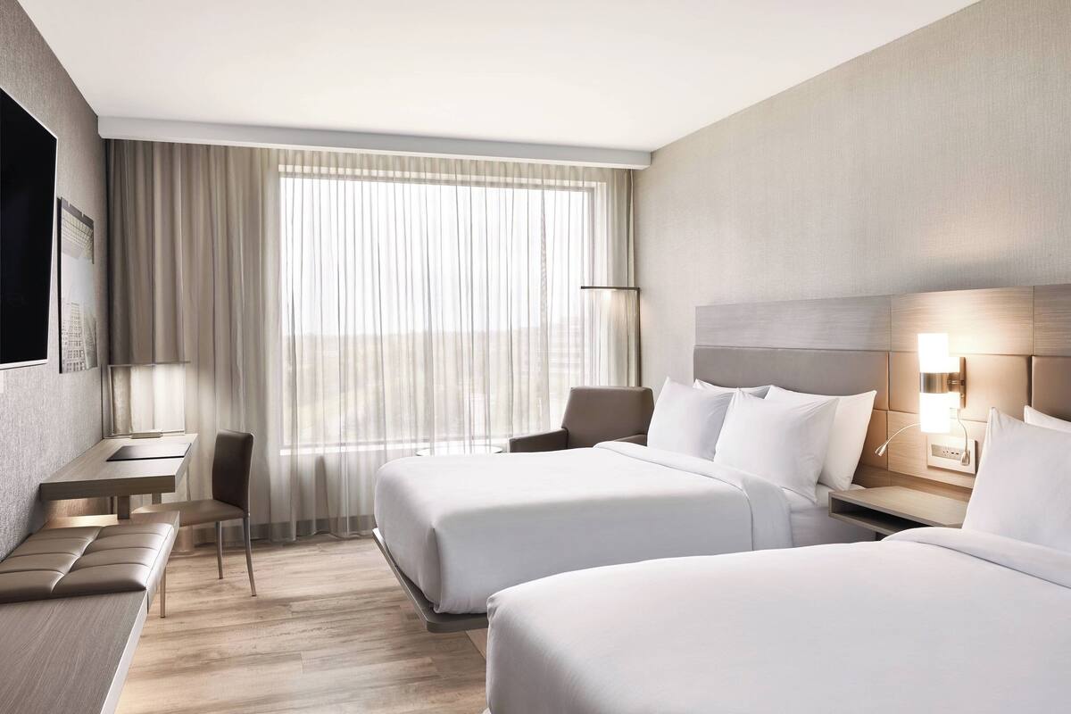 A hotel room with two beds, a desk, and a chair.