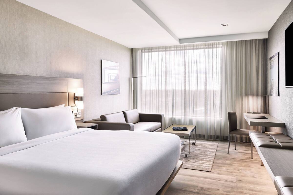 A modern hotel room with a large bed, a sofa, a desk, and a chair.