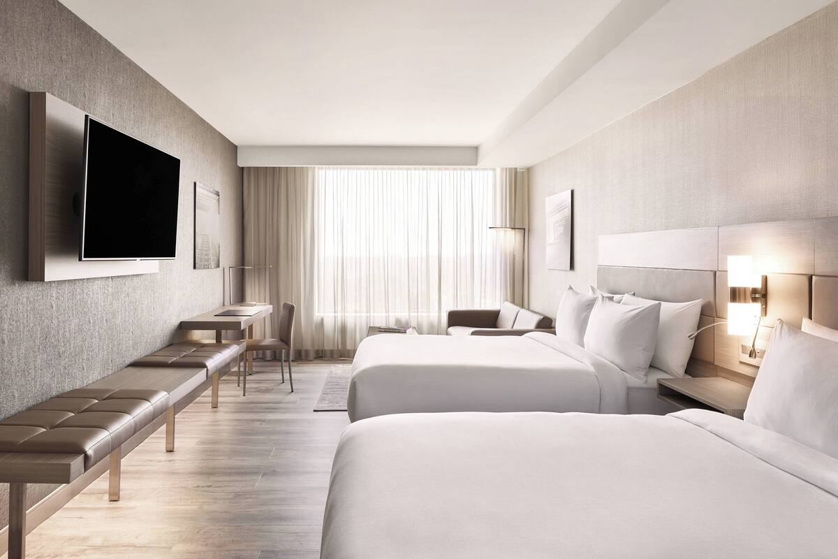 A modern hotel room with two beds, a TV, a desk, and a seating area.