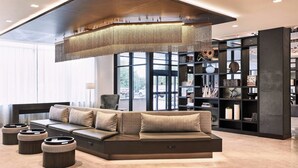 A modern living room with a sectional sofa, a large bookshelf, and a decorative ceiling light. - AC Hotel Bridgewater (Bridgewater)