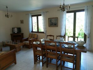 A dining area with a wooden table set for four, surrounded by chairs. There is a television on a stand to the left.