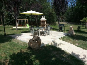 An outdoor patio with a table and chairs, a swing set, and a barbecue grill.