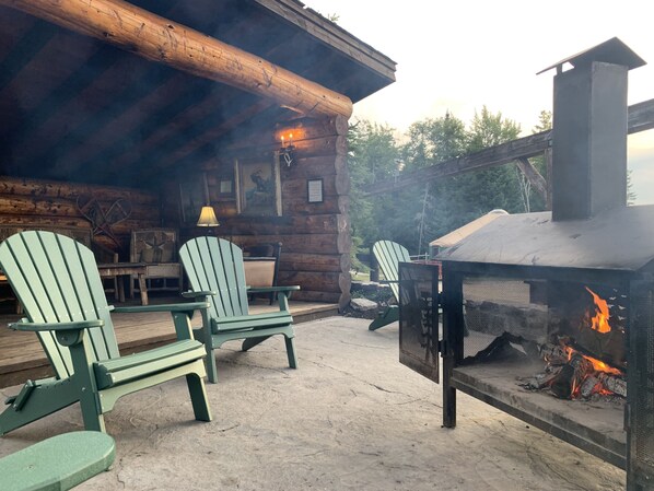 A rustic cabin with Adirondack chairs, a fireplace, and a log wall.