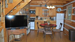 A cozy cabin-style kitchen with a wooden staircase, a dining area with a red table, and a TV on a wooden stand. - Sweet Retreat-NC cabin with mountain & river views, firepit, Smart TV, River Tubes, (Jefferson)