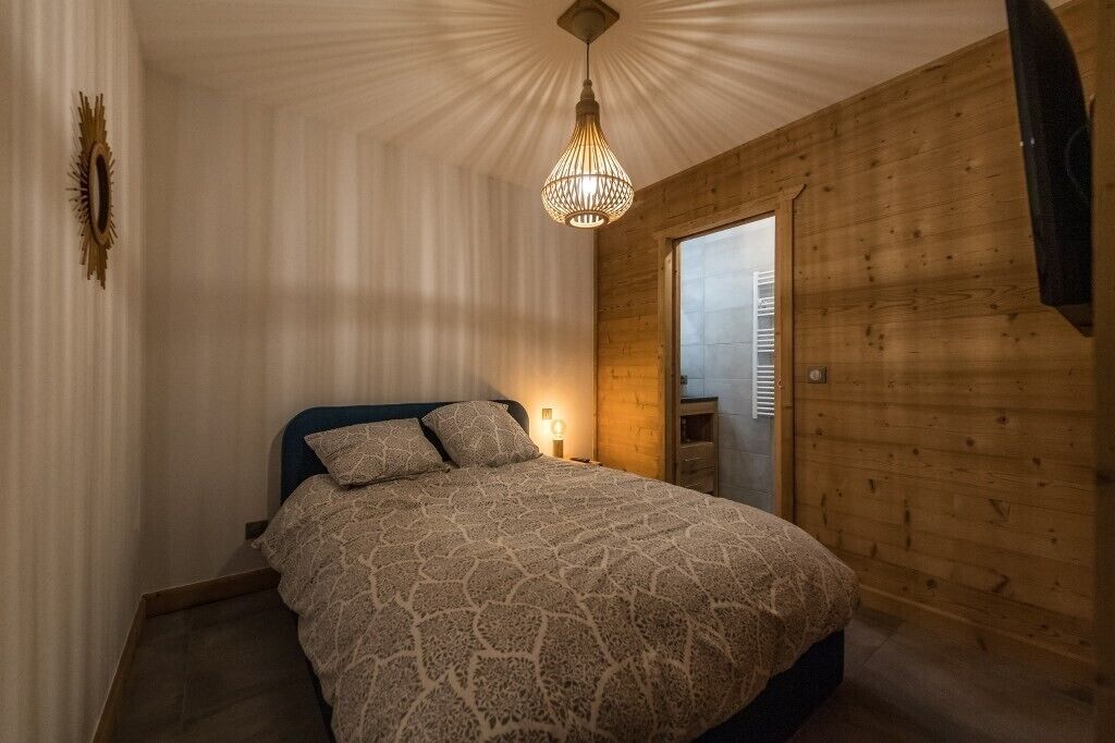 Ett sovrum med en säng, en hängande lampa, en trädörr och ett fönster.