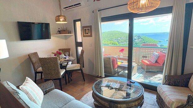 Een woonkamer met een bank, stoelen, een ronde salontafel, een televisie, en een balkon met uitzicht.