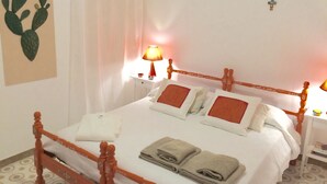 A neatly made bed with pillows and folded towels, a bedside lamp, a wall decoration, and a nightstand with a small bowl.
