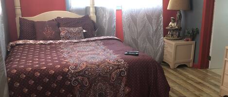 A bedroom with a large bed, a red rug, a nightstand with a lamp, and a window with curtains.