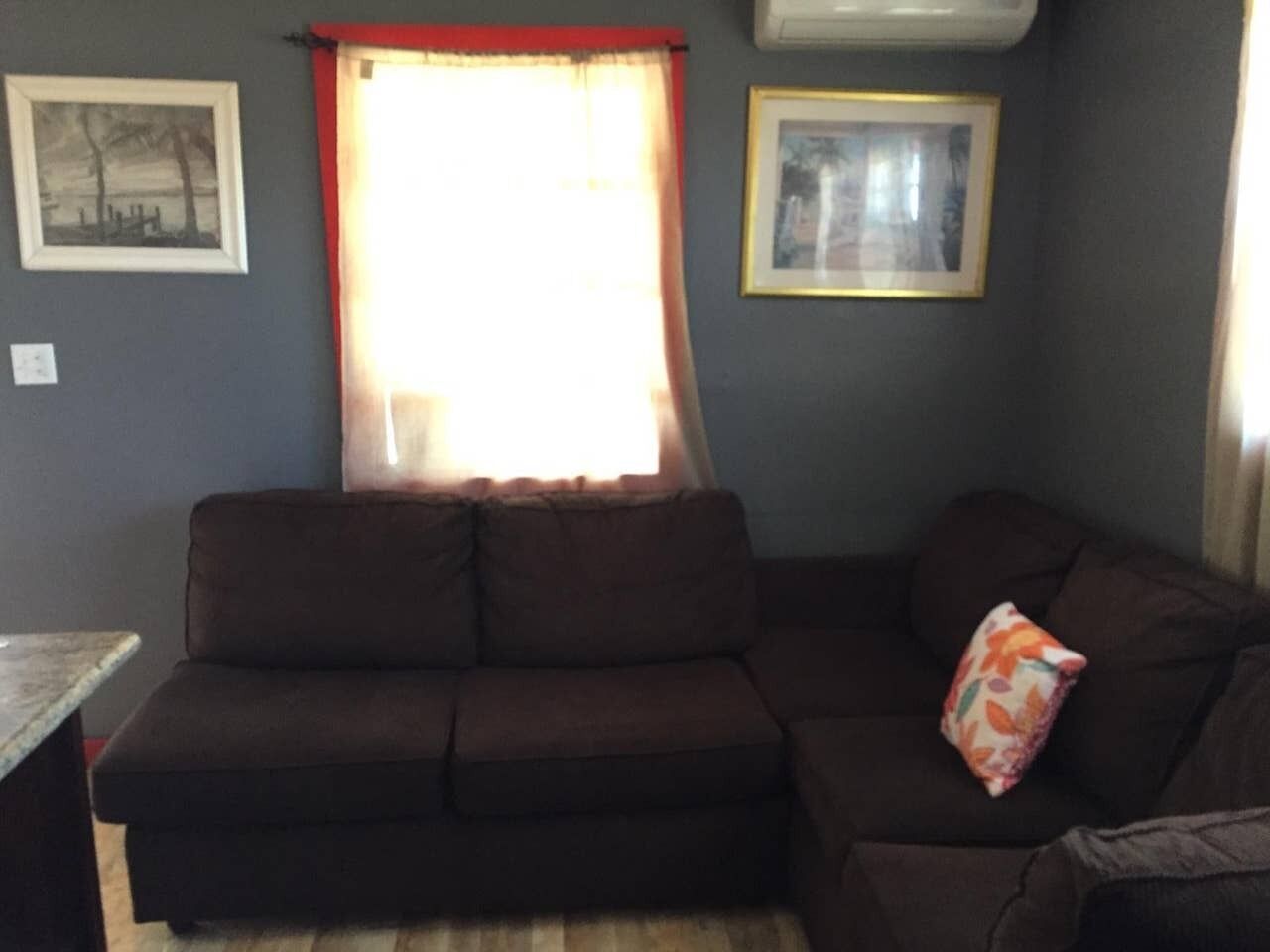 A living room with a brown sofa, a small table, and two framed pictures on the wall.