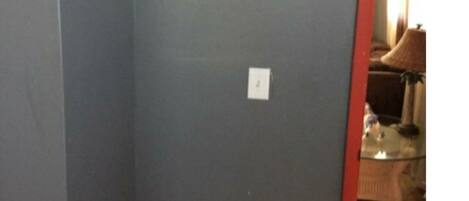 Une pièce avec un mur gris, un téléviseur à écran plat fixé au mur, une prise de courant et un chambranle rouge donnant accès à une autre pièce.