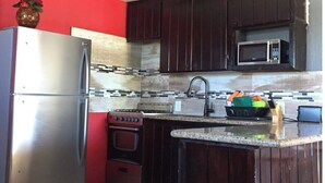 A kitchen with dark wooden cabinets, a stainless steel refrigerator, a microwave, a stove, and a ceiling fan. - Cozy  apartment with beach 7 mins drive away. CAR RENTAL , A.C , CABLE,WIFI, (George Town)