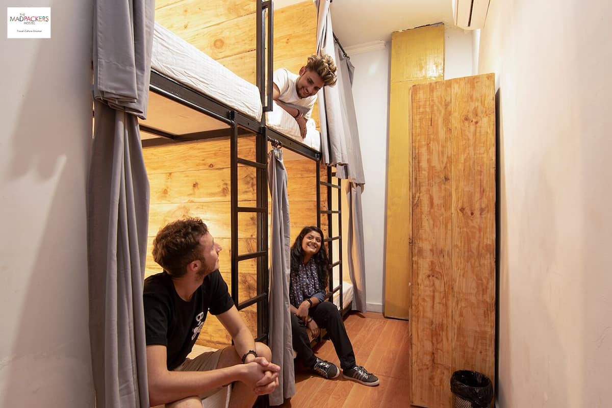 A dormitory room with bunk beds, wooden flooring, and a door.