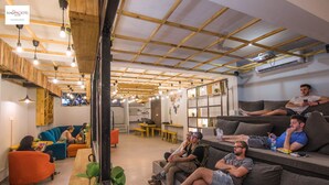 A hostel interior with wooden beams, multiple seating areas, and a kitchenette. - Madpackers Hostel Agra (Agra)