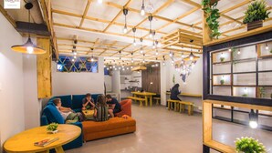 A modern interior with wooden beams, hanging lights, a sofa, tables, and potted plants. - Madpackers Hostel Agra (Agra)