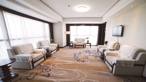 A spacious living room with a large window, a flat-screen TV mounted on the wall, and a patterned carpet. - Days Hotel & Suites by Wyndham Jiangsu Xinyi (Xuzhou)
