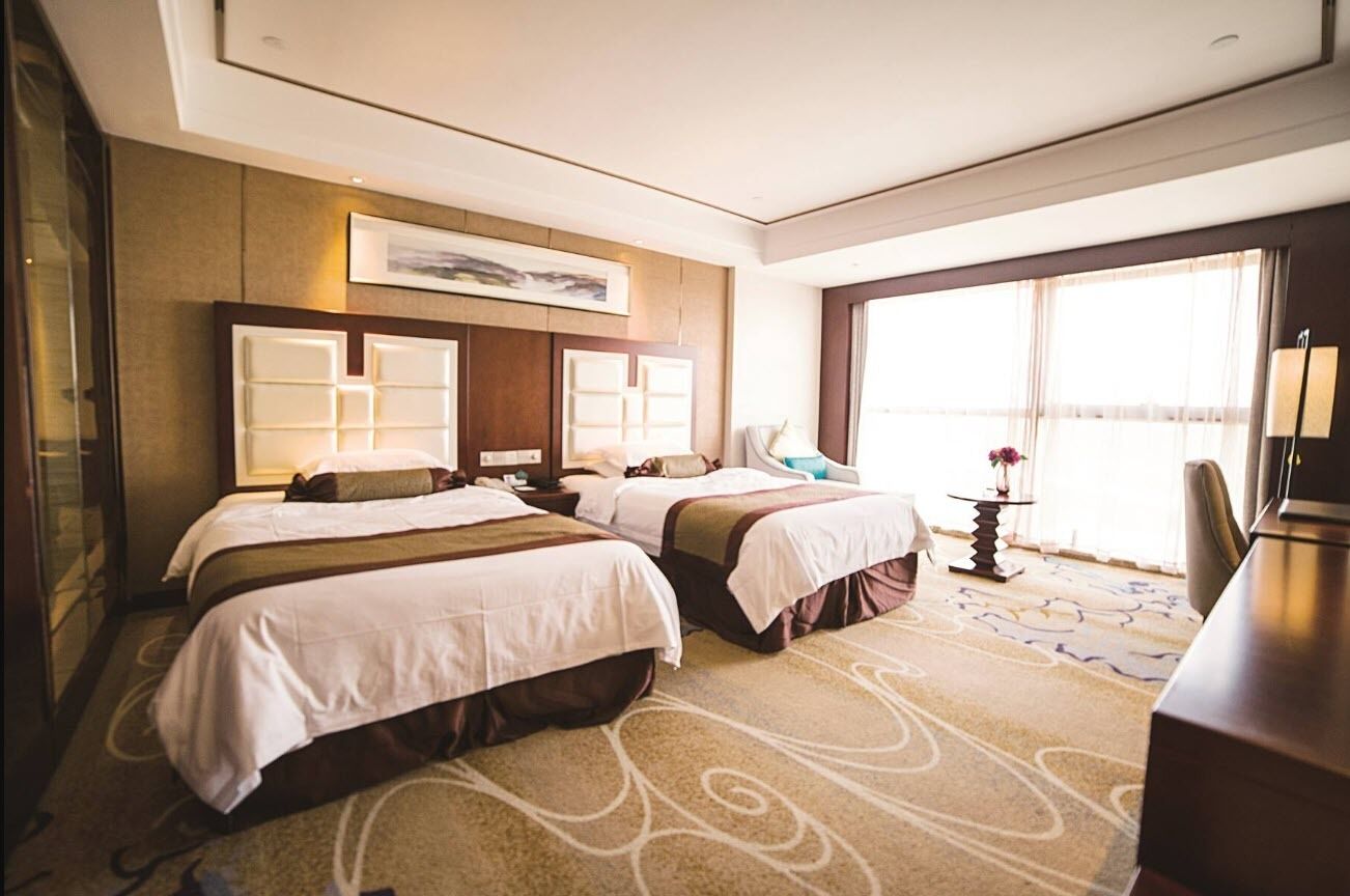 Una habitación de hotel con dos camas, un ventanal amplio, un escritorio y una silla.