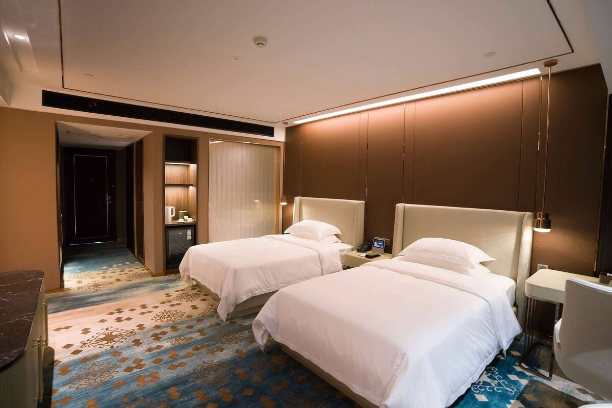 A hotel room with two beds, a desk, a chair, a nightstand, and a bathroom with a shower and toilet.