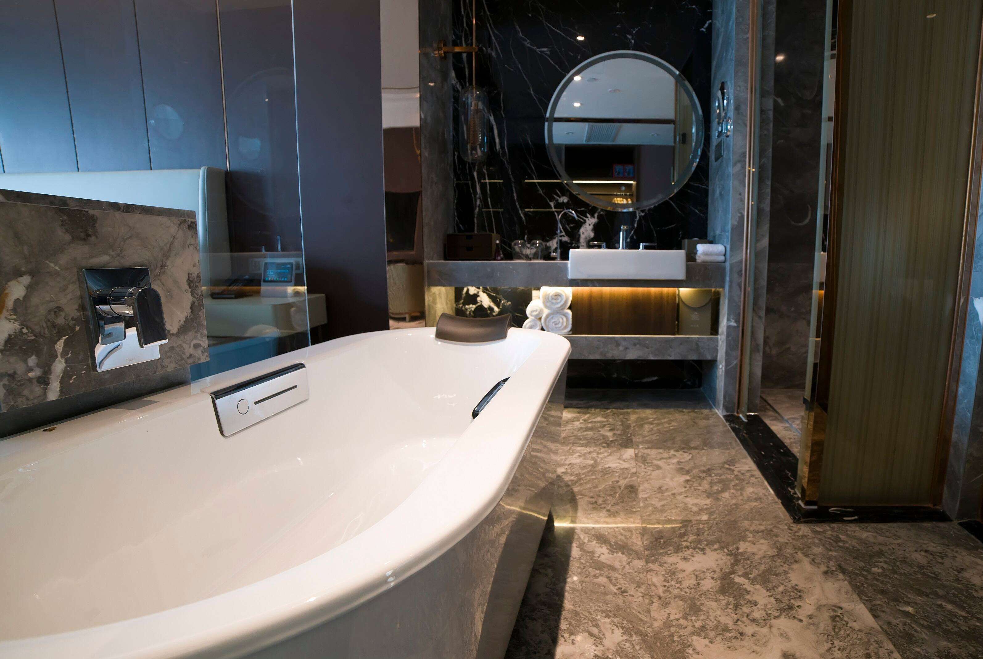 Un baño moderno con una bañera grande, un espejo redondo y encimera de mármol.
