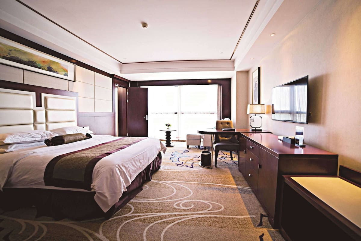 A hotel room with a large bed, a desk, a chair, a TV, and a window with curtains.