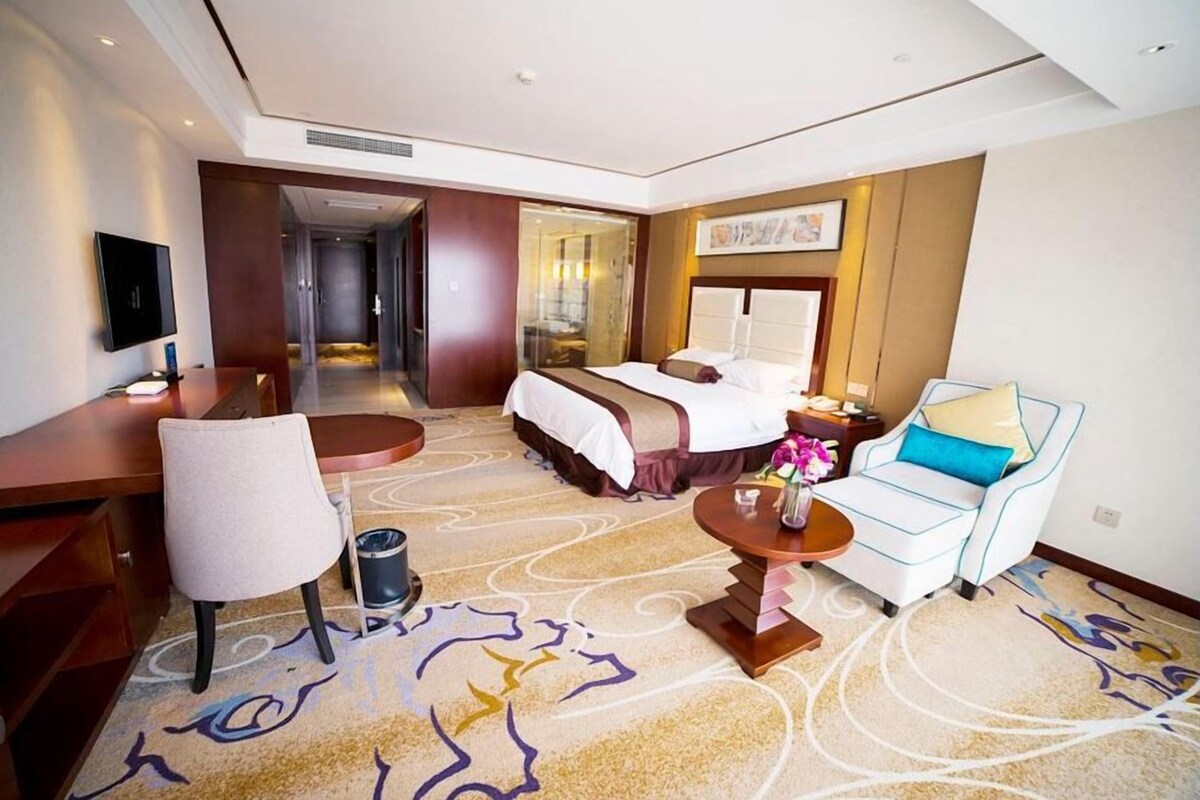 A hotel room with a bed, a desk, a chair, a sofa, and a small table with a vase of flowers.