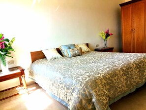 Un dormitorio con una cama, un armario de madera, una mesita de noche y un jarrón con flores.