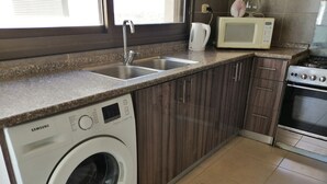 Une cuisine équipée d’un lave-linge, d’un four à micro-ondes, d’un évier et d’une cuisinière.