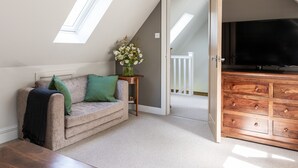 Ein Schlafzimmer im Loft-Stil mit schrägverdeckter Decke, einer Couch mit grünen Kissen, einer Holzkommode und einem Fernseher.