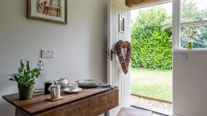 Eine Küche mit einem Holztisch, zwei Hocker, einem Blumentopf und einem gerahmten Bild an der Wand.
