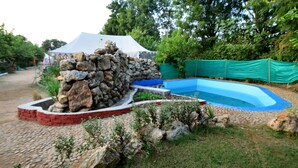 Estructura de piedra con piscina, rodeada de follaje y una tienda de campaña.