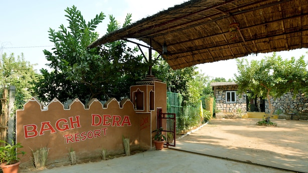 Señal anunciando Bagh Dera Resort, con un edificio de piedra al fondo.