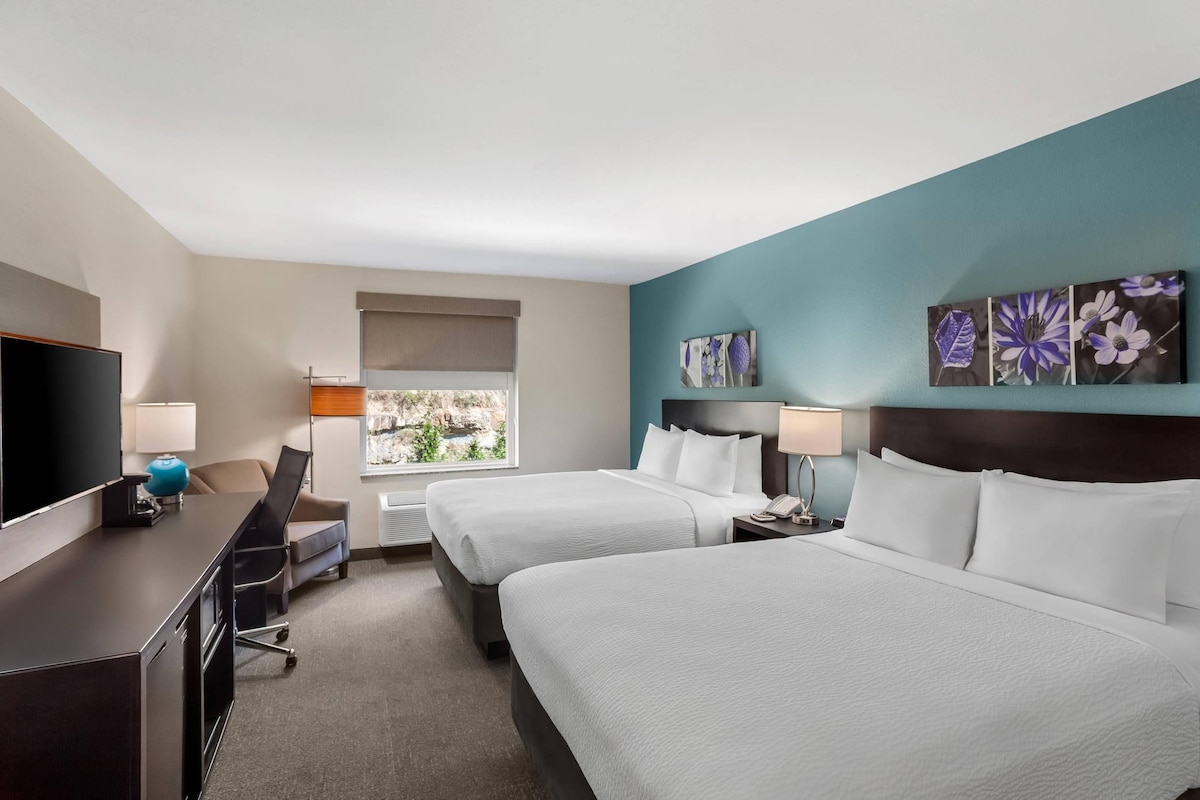 Een hotelkamer met twee bedden, een bureau, een televisie en kunstwerken aan de muren.
