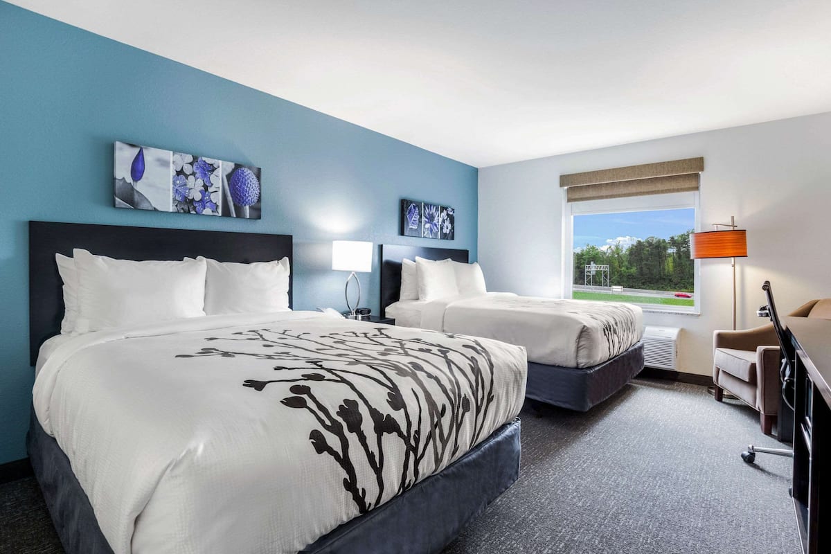 A hotel room with two beds, a desk, a chair, and artwork on the walls.