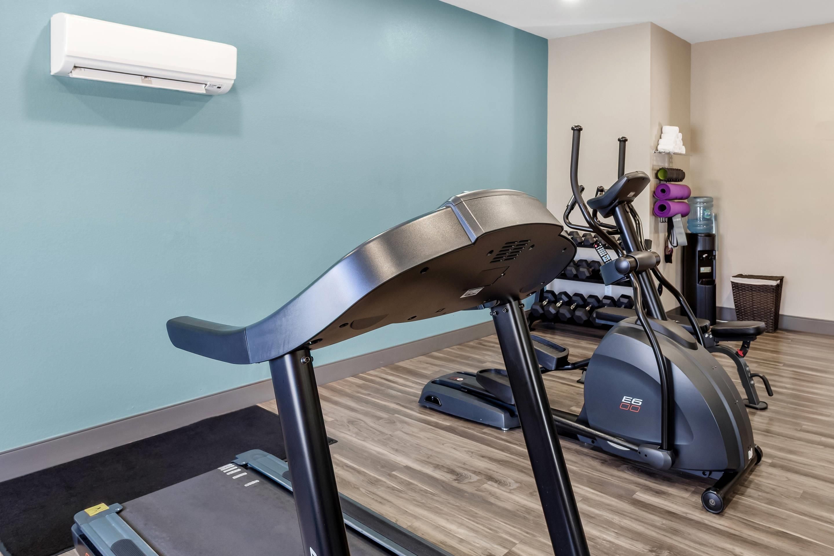 A gym with exercise equipment including a treadmill, elliptical, and weights.