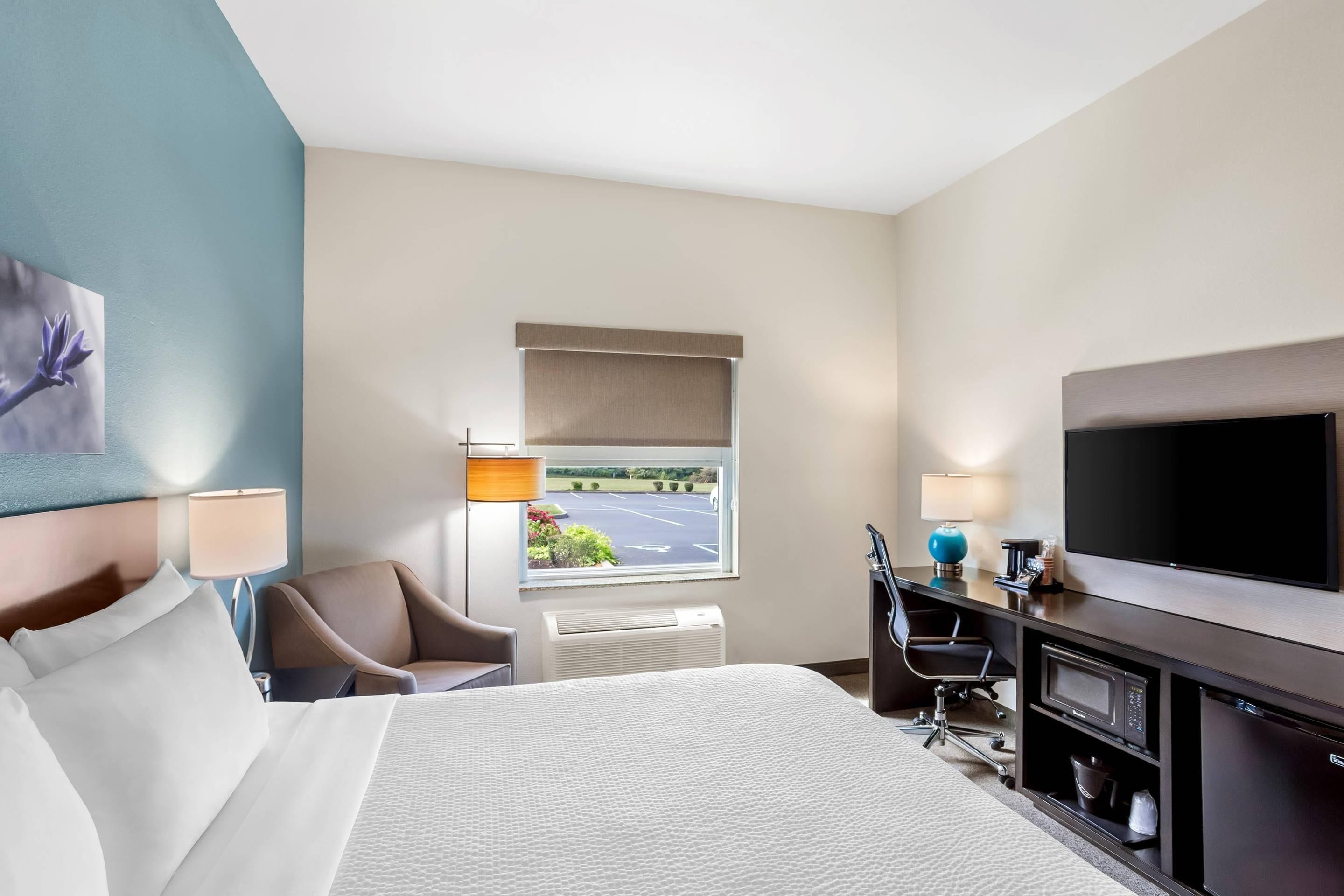 Habitación de hotel con cama, escritorio, televisor y ventana que da a un estacionamiento.