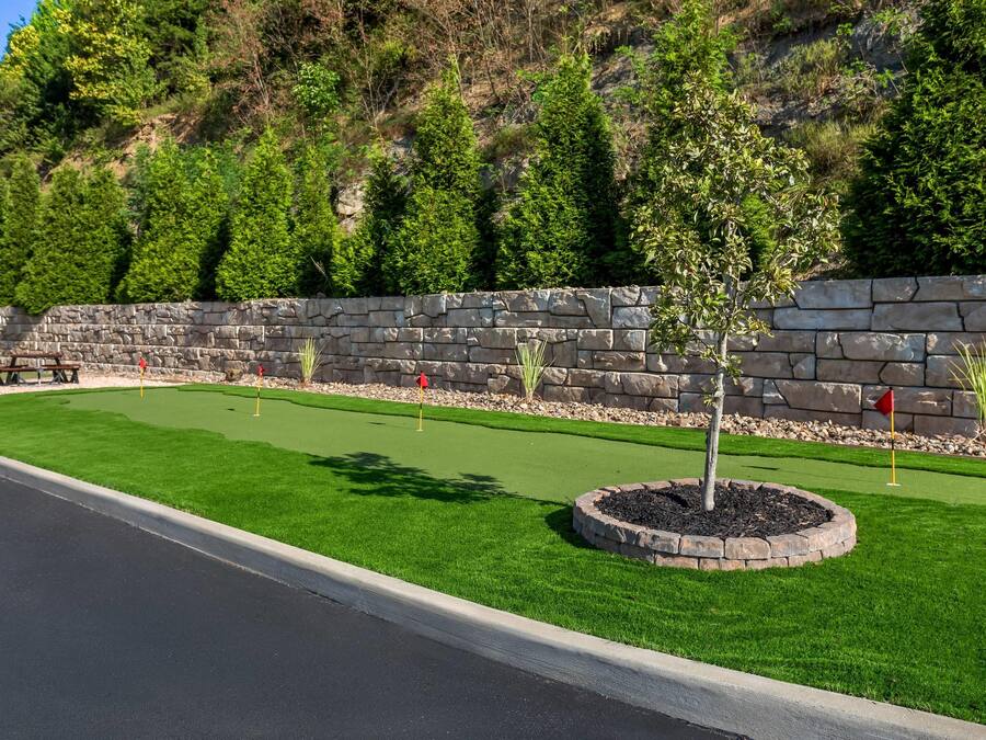 Um campo de golfe bem cuidado, com muro de pedra, fairways verdes e céu claro.