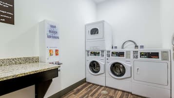 A laundry area with two stacked washers and dryers, a granite countertop, and a sign listing available laundry products.