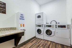 Un área de lavandería con dos lavadoras y secadoras apiladas, una encimera de granito y un letrero que enumera los productos de lavandería disponibles.