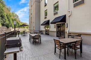 Un patio exterior con mesas, sillas, una parrilla y sombrillas.
