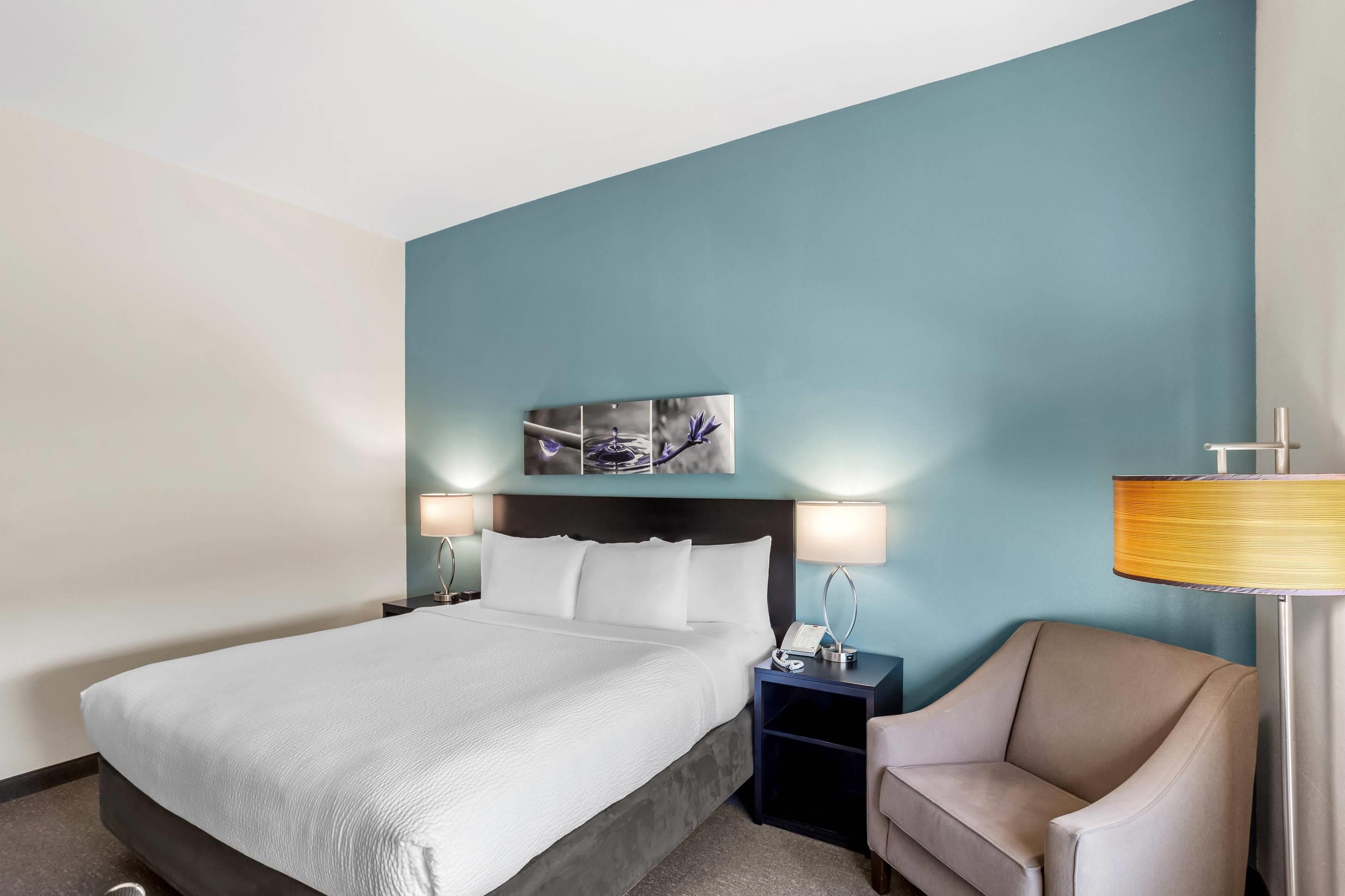 A hotel room with a bed, two bedside tables, a chair, and a wall-mounted lamp.