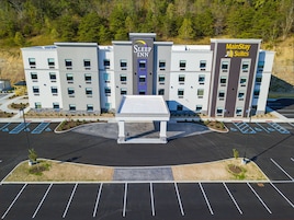 Un hotel con entrada central, varios espacios de estacionamiento y una zona ajardinada con árboles pequeños.