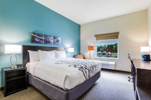 A hotel room with a large bed, two bedside tables, a window with a view, and a desk with a lamp.