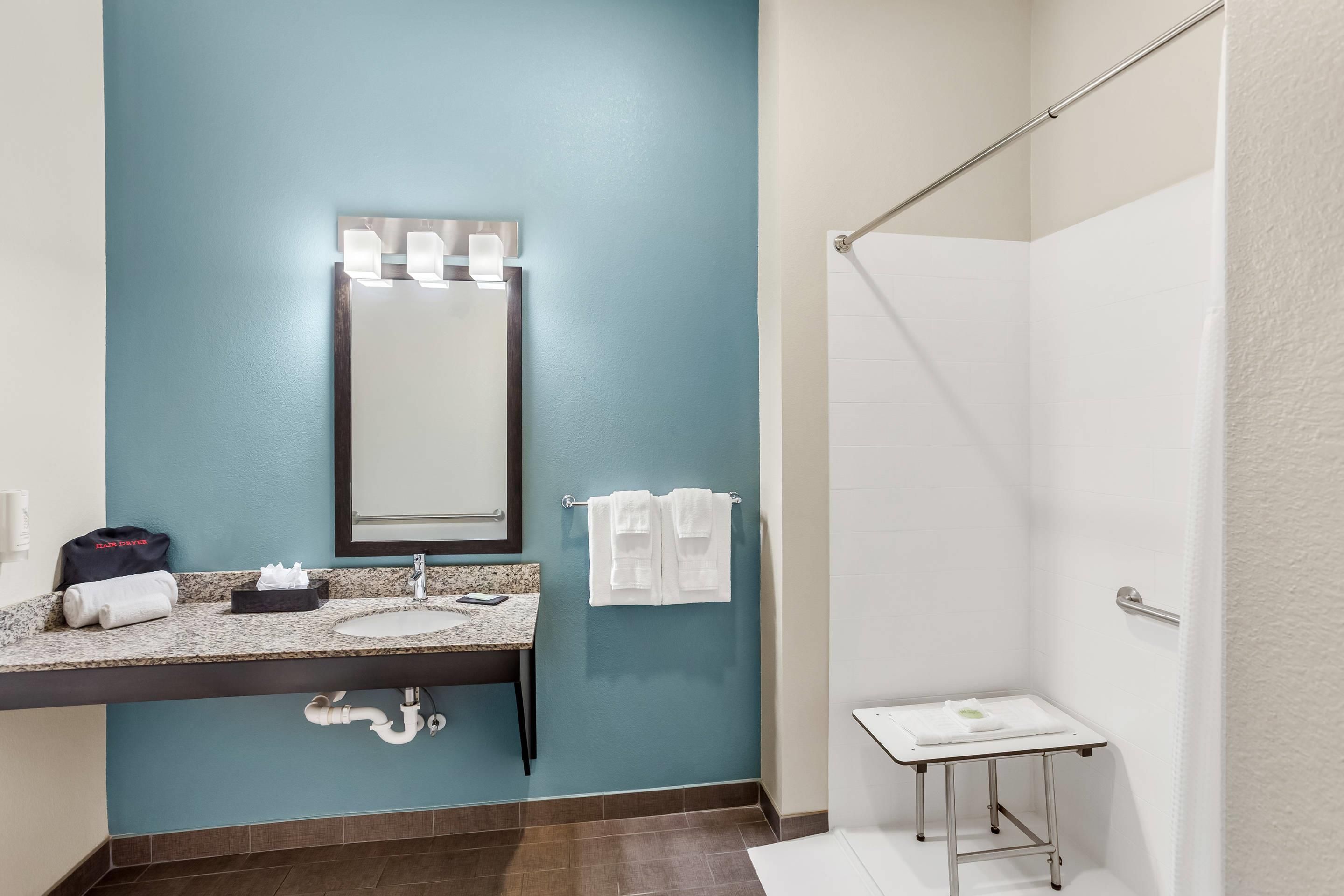 A bathroom with a blue wall, a sink with a mirror, a towel rack, and a shower area.