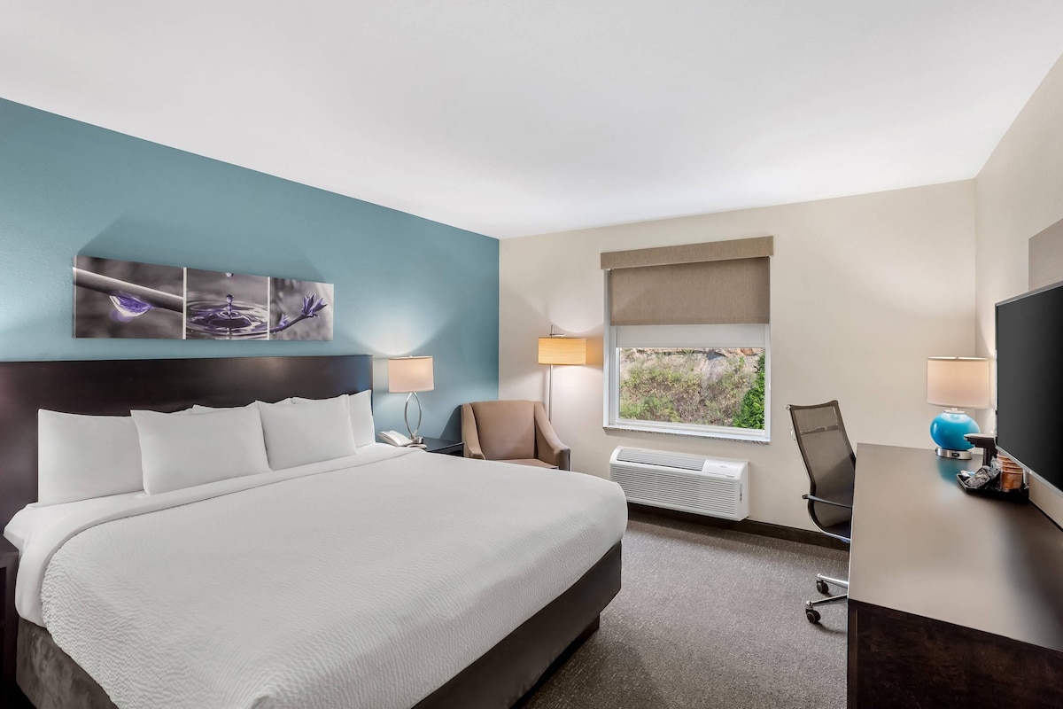 Een hotelkamer met een groot bed, een bureau met stoel, een raam met uitzicht en een kunstwerk aan de muur.