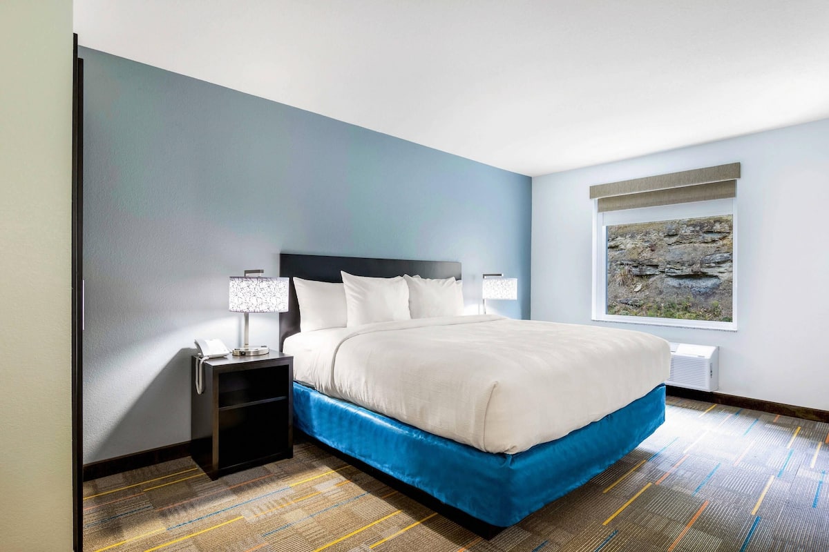 A hotel room with a bed, nightstand, lamp, and a window with a view of rocks.