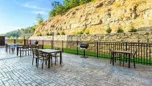 Eine Terrasse im Freien mit Steinböden, Tischen und Stühlen, umgeben von einer Steinmauer und einem Metallzaun.