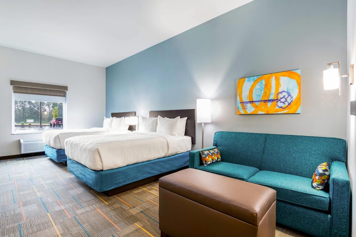 A hotel room with a large bed, a sofa, a small table, and a painting on the wall.