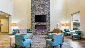 Eine Lobby mit Kamin aus Stein, einem Flachbildfernseher und blauen Sesseln, die um einen Couchtisch angeordnet sind.